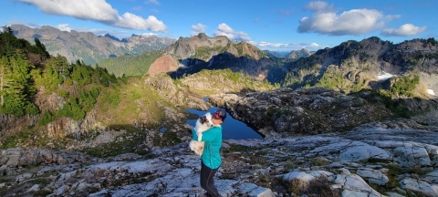 A woman holds a white dog with majestic mountains in the background