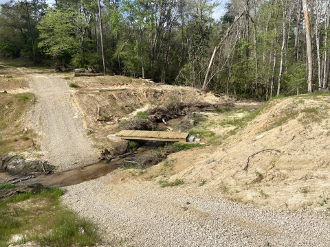 A gravel road through a small stream with a bridge over it