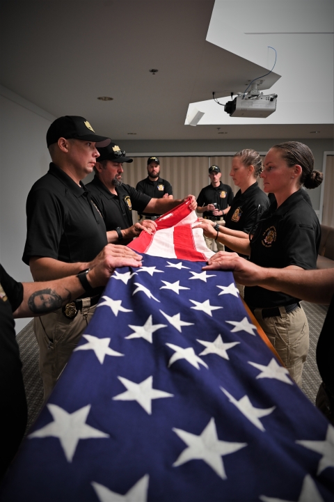 The honor guard stands together to fold an American flag. There are two people on each side of the flag.