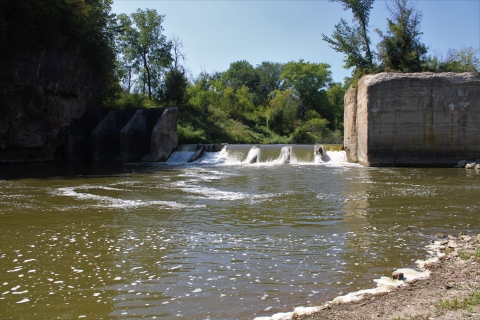 Water pours down a dam into a pool like area in the river.