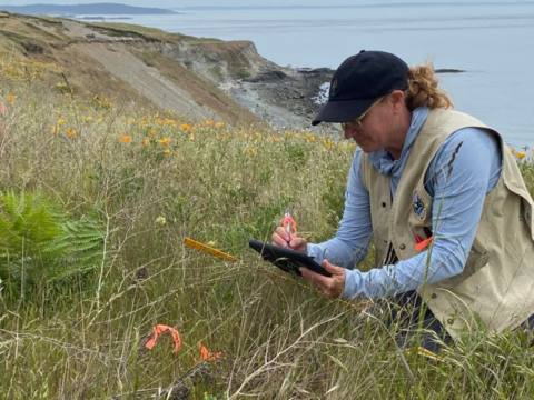 Julie Combs writes on clipboard while looking at vegation. 