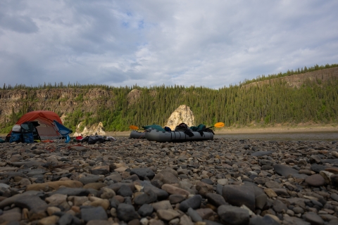 a tent and small rafts on a gravel bar along a river