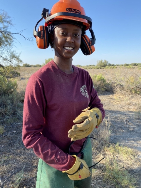 A woman wearing protective gloves and an orange protective hard hat with headphones