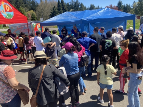 A crowd of people gather around and in several tents providing shade