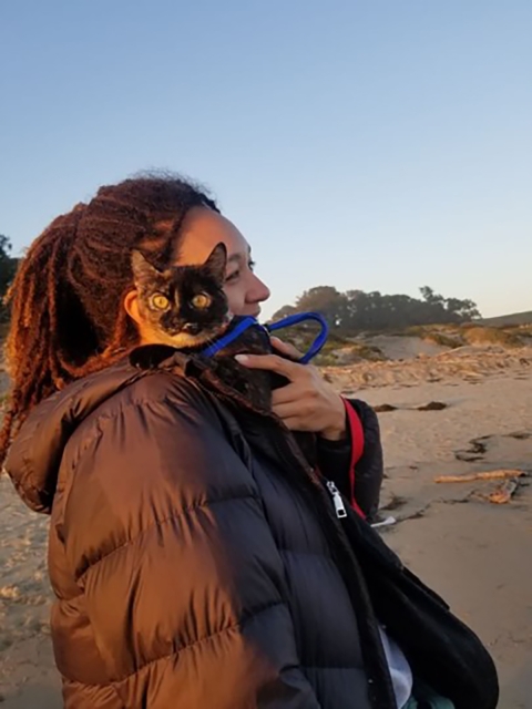 A woman wearing a puffy black jacket and holding a cat looks off into the distance