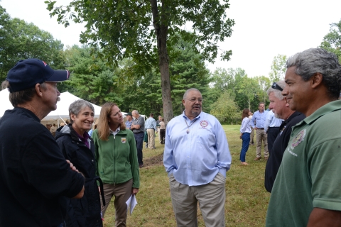 A man in a Mashpee Wampanoag long sleeve shirt stands with 5 adults in various conservation uniforms. 