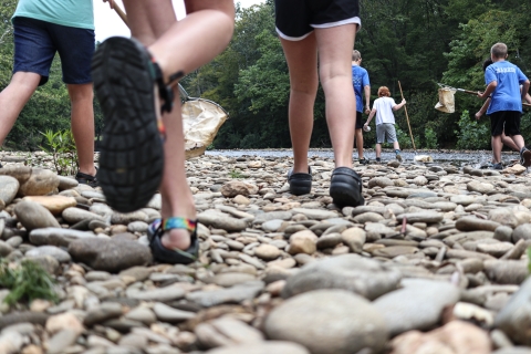 Several kids running toward a shallow river, some holding nets