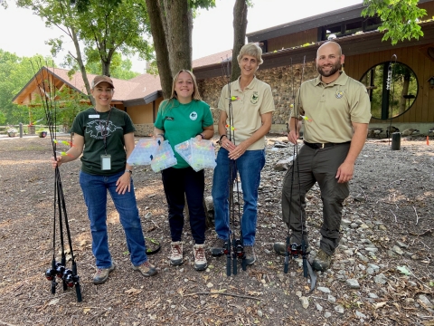 Four adults stand in front of a building holding fishing tackle.