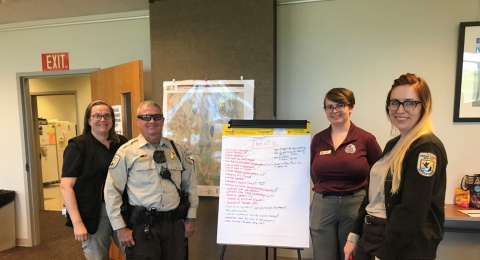 Four people standing by a white board with writing on it.