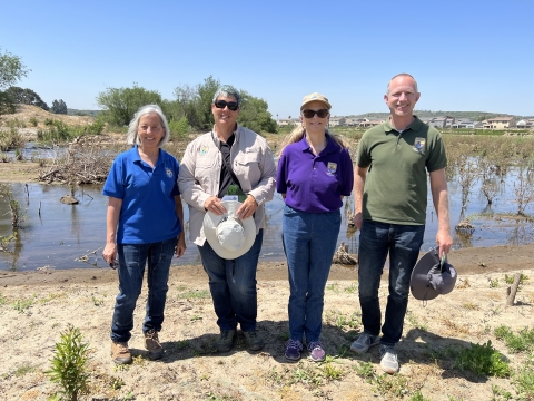 three woman and one man stand in front of creek