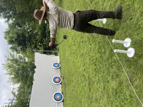 a park ranger aims a bow at archery targets outside