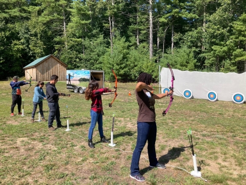 a group of kids aim their bows at archerty targets