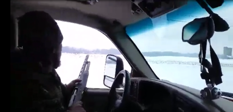 a man points a hunting rile out the window of a truck