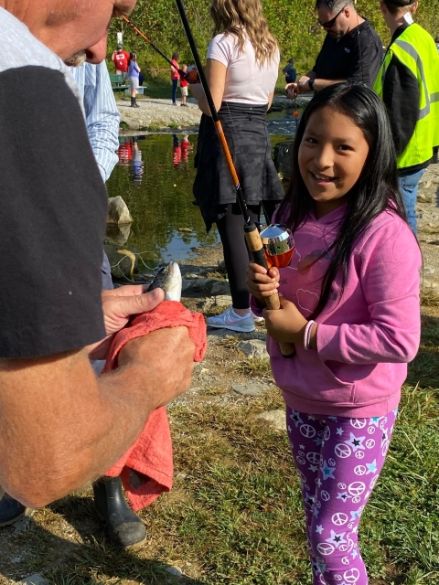 Little girl smiling with a fishing pole in front of a stream