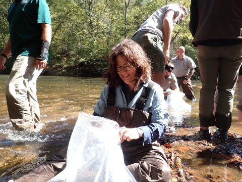 People in a shallow river holding plastic bags