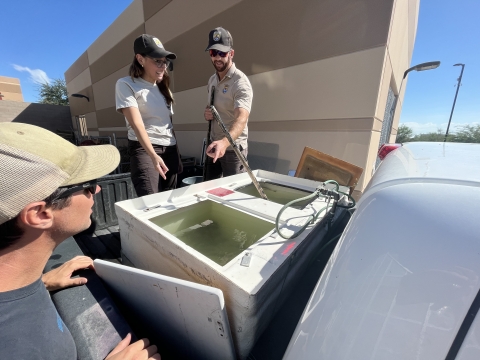 Two Service employees show a teacher the fish tanks in the back of a truck.