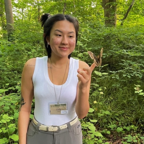 A woman smiles while looking at a butterfly perched on her finger