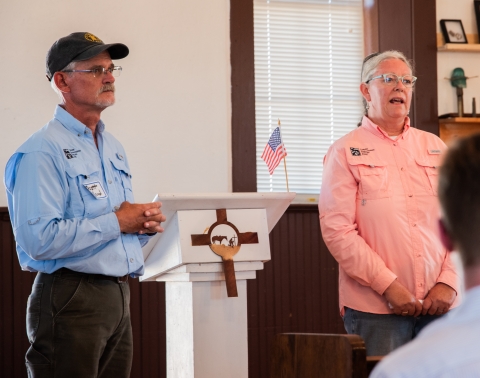 Two people stand in front of a podium addressing an audience.