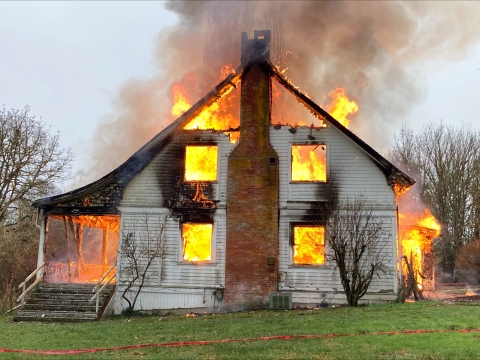 A two story house is on fire, dark smoke rises from the flames. 