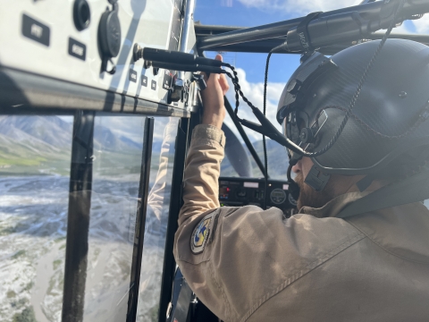 A refuge Law enforcement officer/pilot looks out the window of a Top Cub bush plane surveying the braided river below which is just out of focus. 