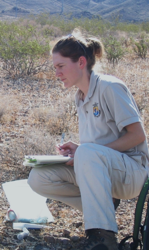 woman with clipboard kneels down on desert ground