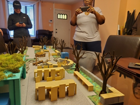 A table topped with a diorama meant to imitate the garden in the foreground with two people in the background.