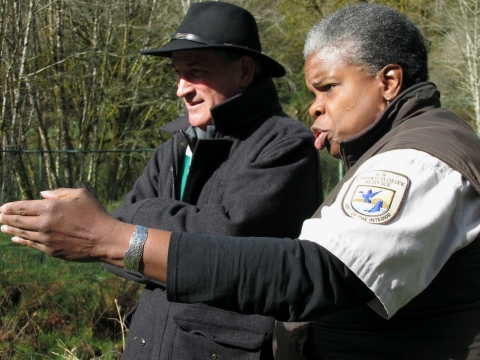 A woman and a man look in the distance as she points with her hand while talking. 