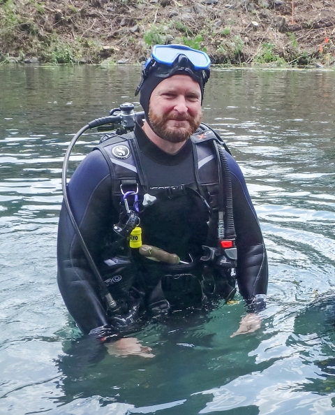 Justin Crow in dive gear, standing in a river. 