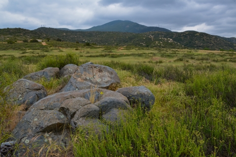 An overcast, gloomy day on San Diego NWR. Boulders on the bottom left followed by hills and a distant mountain.