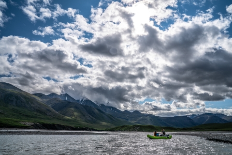 rafters float a wide river with mountains and blue sky in back