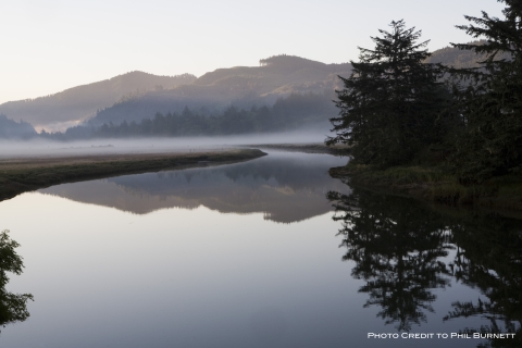 A scene of the Siletz Bay with trees and mountain in the background