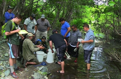 a group of people standing in an next to a stream looking in white buckets
