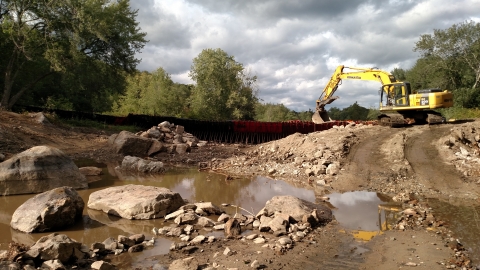 muddy, rocky riverbed with excavator on hill on right