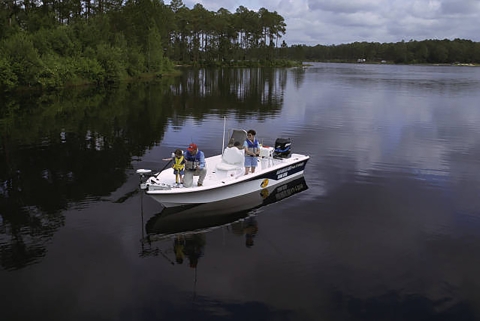 Family fishing in a boat on a body of water with woody landscape in the background. 