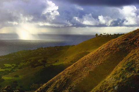 vegetated land sloping towards the Pacific Ocean with rays of sunlight appearing through clouds