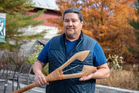 up close image of man holding wooden spear with fall leaves in background