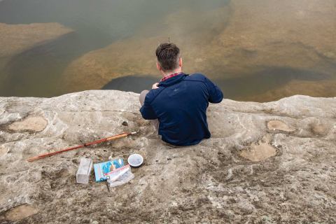 Adam Comer from TPWD sets up microfishing gear on rocky shore. 