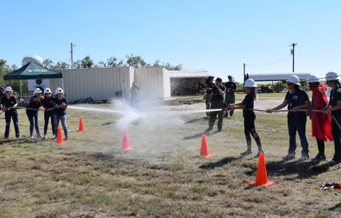 2 groups of people face ech other holding fire hoses whose spray hits the other