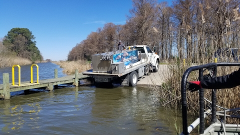 A truck with a large metal tank banks into a boat launch.