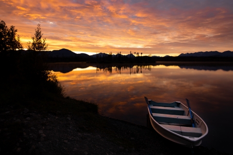 A sunset on a lake with a rowboat on shore