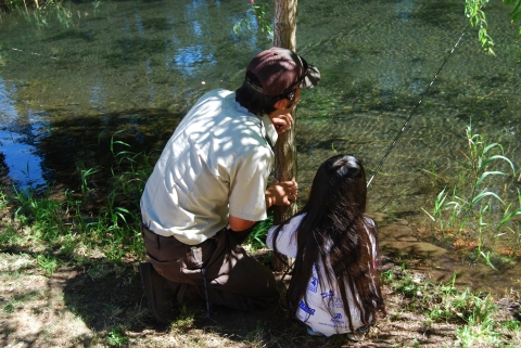 Adult and child fishing, crouched along the bank, looking out into the water