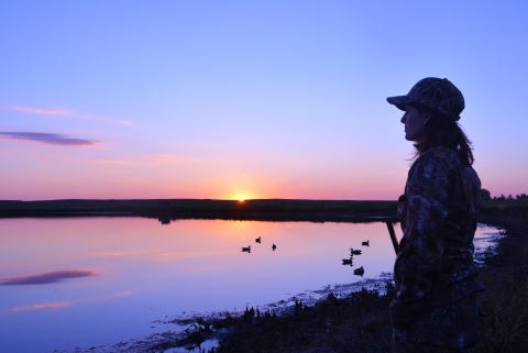 person waterfowl hunting by a wetland at sunrise