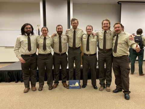 Seven recent graduates of the wildland fire apprentice program pose for a photo in their uniforms