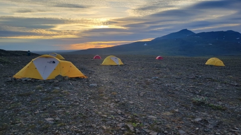 sunset with tents in the foreground and mountains in the background