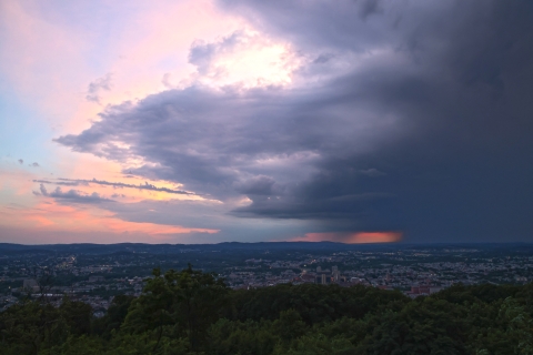 Wide view from a hill overlooking a city with hills in the background at sunset. 