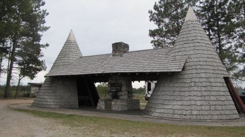 A structure that looks like two teepees with a roof between them and a stone fireplace inside.