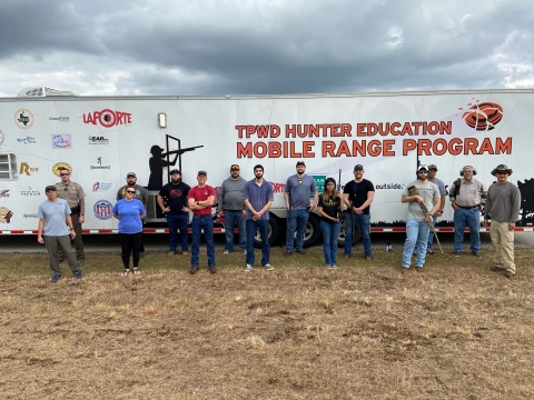 Shooting sport youth participants and mentors stand in front of the white Hunter Education Mobile Range Trailer