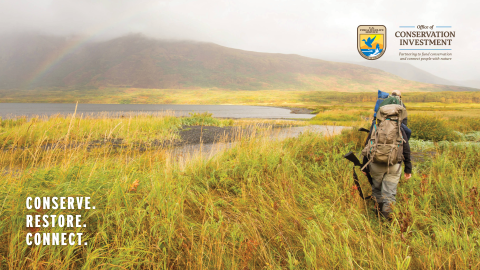 Two hunters with backpacks and firearms walk through Kodiak National Wildlife Refuge.