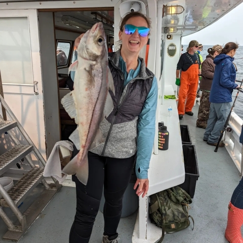 a woman stands on a boat wearing sunglasses and holding a very largefish