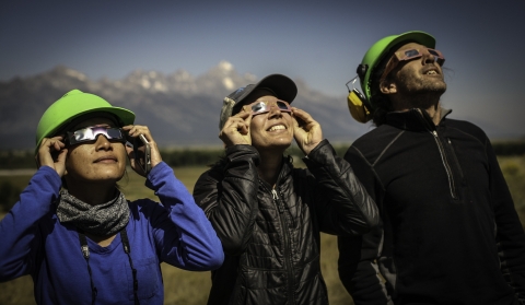 Three people wearing special eclipse glasses, stare up